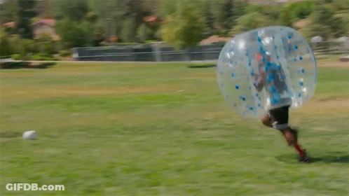 Two People Are Playing Bubble Soccer In A Field GIF