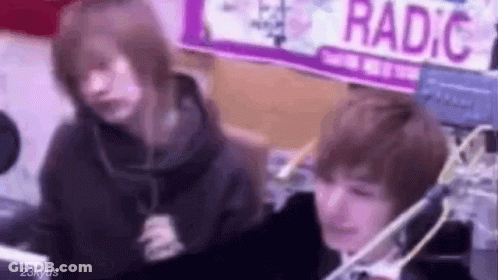 Two People Are Sitting In Front Of A Microphone In A Room . GIF