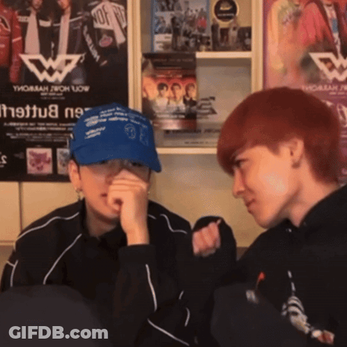 Two People Are Sitting In Front Of A Wall With A Poster That Says Thomas Now GIF