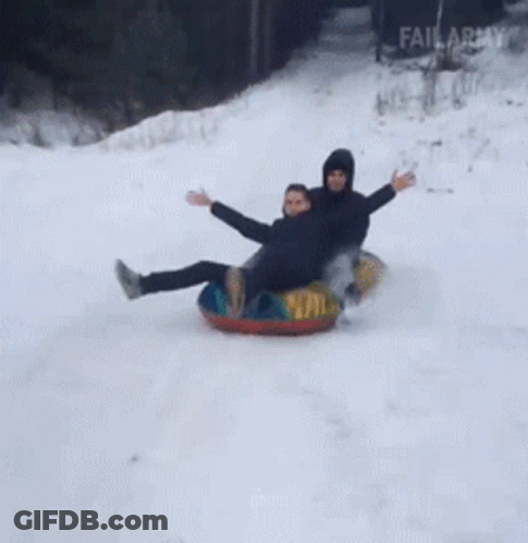 Two People Are Sledding Down A Snowy Hill On Tubes GIF