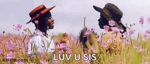 Two People Are Standing In A Field Of Flowers . GIF