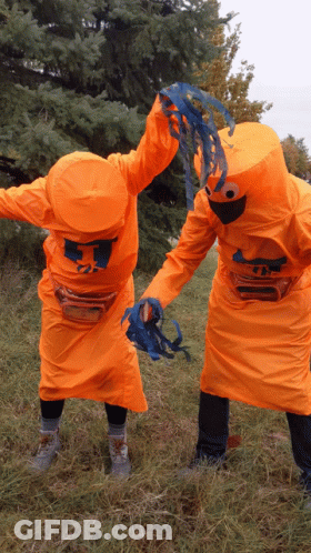 Two People In Orange Costumes With The Letter T On Their Heads GIF