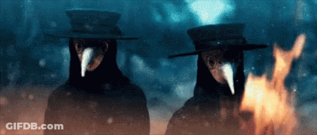 Two People In Plague Masks And Hats Beside Fire GIF