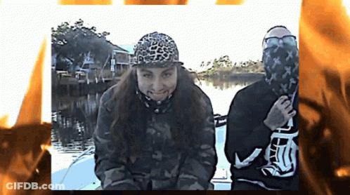 Two People On A Boat With One Wearing A Leopard Print Hat And The Other Wearing A Black Shirt With The Letter T On It GIF