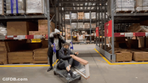 Two People Pushing Cart In Warehouse With Gtu Sign GIF