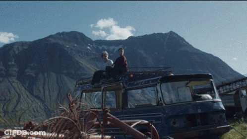 Two People Sit On The Roof Of A Blue Van GIF