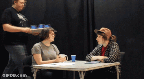 Two People Sitting At Table With Man Holding Tray GIF