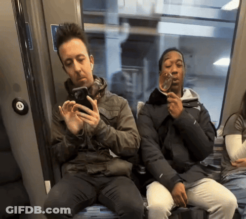 Two People Sitting On A Train With One Holding A Glass GIF