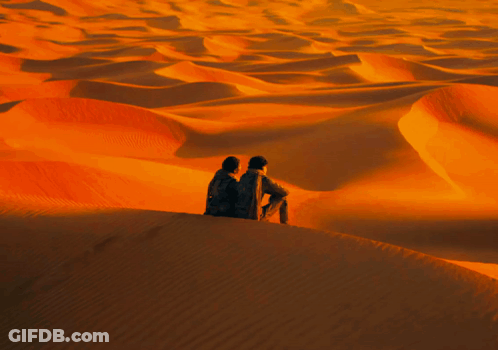 Two People Sitting On Sand Dune In Desert GIF
