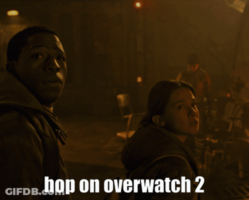 Two People Standing In Front Of A Fire With The Words Hop On Overwatch 2 Below Them GIF