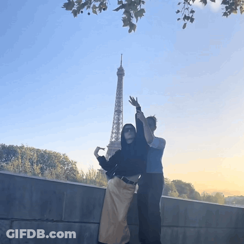 Two People Standing In Front Of The Eiffel Tower With Their Arms In The Air GIF