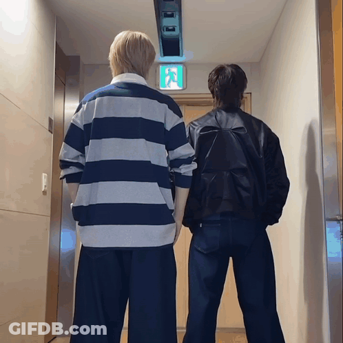 Two People Standing In Hallway With Exit Sign GIF