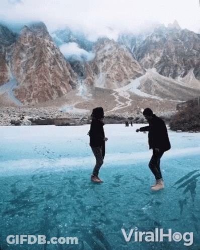 Two People Standing On A Frozen Lake With Mountains In The Background And The Words Viralhog On The Bottom Right GIF