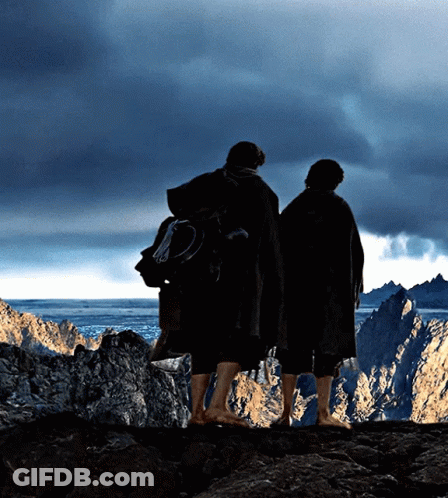 Two People Standing On Top Of A Rocky Cliff Looking Out Over A Body Of Water GIF