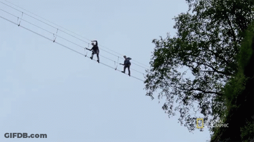 Two People Walking Across Rope Bridge With National Geographic Logo GIF