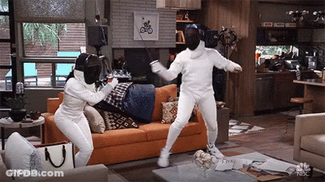 Two People Wearing Fencing Masks Are Standing In A Living Room . GIF