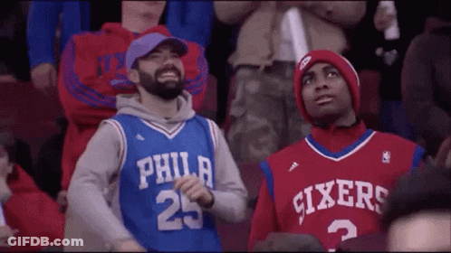 Two Philadelphia Sixers Fans Are Sitting In The Stands At A Basketball Game . GIF