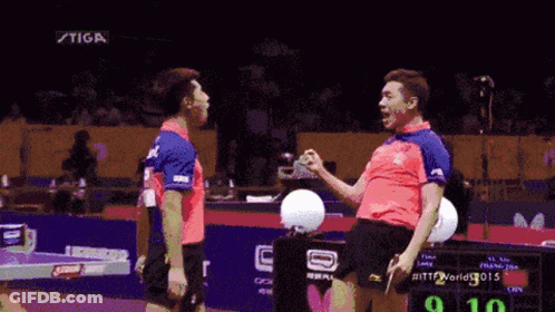 Two Ping Pong Players Are Standing Next To Each Other In Front Of A Scoreboard That Says Stiga GIF