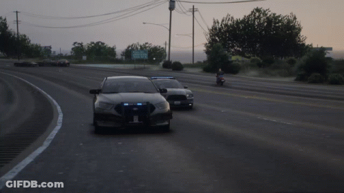 Two Police Cars Are Driving Down A Road With A Sign In The Background That Says Kings County GIF