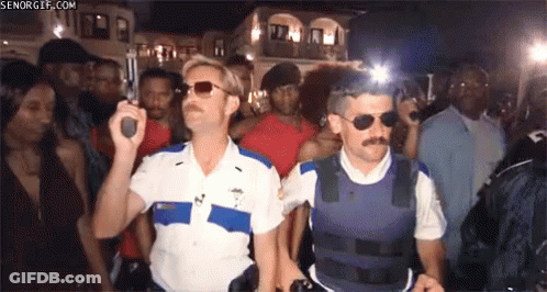 Two Police Officers Are Standing In Front Of A Crowd Holding Guns .. GIF