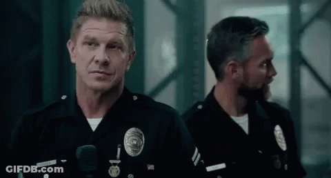 Two Police Officers Are Standing Next To Each Other In A Dark Room Looking At The Camera . GIF