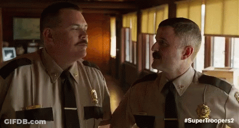 Two Police Officers Are Standing Next To Each Other In A Hallway Talking To Each Other . GIF
