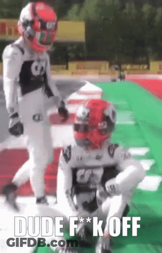 Two Race Car Drivers Are Standing On A Race Track And One Of Them Is Sitting On The Ground . GIF
