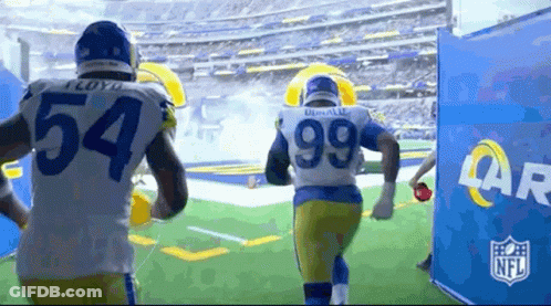 Two Rams Football Players Are Running On The Field During A Game . GIF