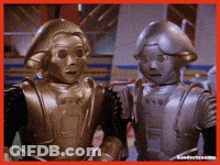 Two Robots Are Standing Next To Each Other And Looking At The Camera GIF
