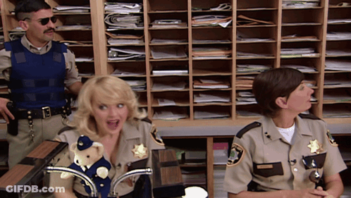 Two Sheriff 'S Officers Are Sitting At A Desk With A Teddy Bear On It GIF
