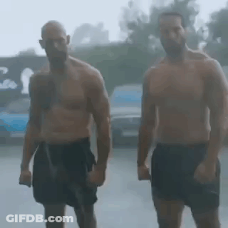 Two Shirtless Men Are Standing In The Rain Holding Hands . GIF