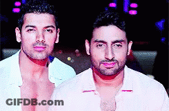 Two Shirtless Men Are Standing Next To Each Other In A Dark Room GIF