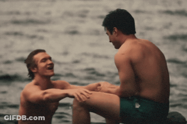 Two Shirtless Men Sitting In Water Talking GIF