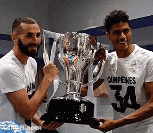 Two Soccer Players Are Holding A Trophy In Their Hands . GIF