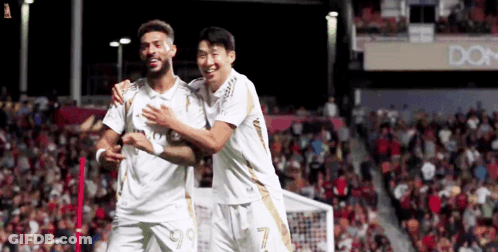 Two Soccer Players Are Hugging Each Other On A Field GIF