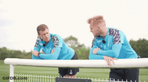 Two Soccer Players Are Leaning On A Fence Talking GIF
