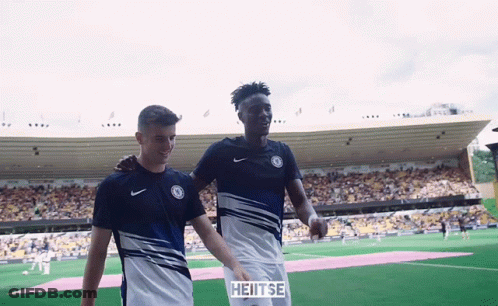Two Soccer Players Are Walking On A Field With A Sign That Says Heitse On It GIF