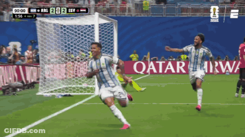 Two Soccer Players Celebrate A Goal In Front Of An Ad For Qatar GIF
