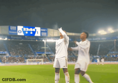Two Soccer Players On A Field With A Scoreboard In The Background That Says 23:58 GIF