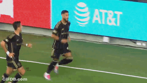 Two Soccer Players Running On A Field With An At & T Sign In The Background GIF