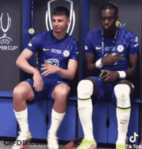 Two Soccer Players Sitting On Bench In Locker Room GIF