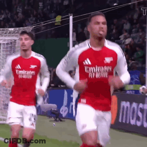 Two Soccer Players Wearing Emirates Airlines Jerseys Are Running On A Field GIF