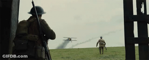 Two Soldiers Are Standing In A Field Looking At A Plane Flying Overhead GIF