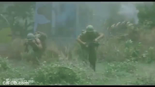 Two Soldiers Are Walking Through A Field Carrying A Rifle . GIF