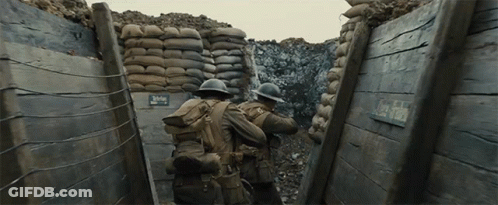 Two Soldiers Are Walking Through A Trench With A Sign That Says Clay Field On It GIF