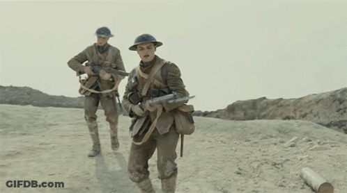 Two Soldiers Wearing Helmets And Carrying Guns Walk Across A Dirt Field GIF