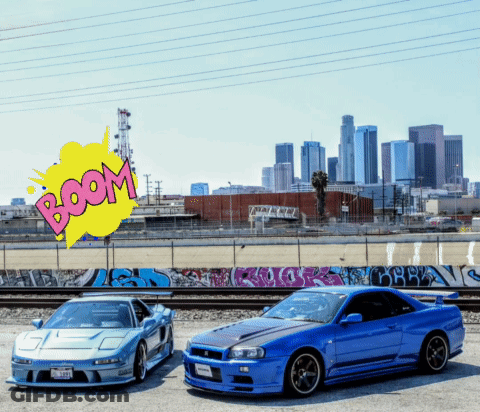 Two Sports Cars Are Parked Next To Each Other With A Boom Sign Behind Them GIF