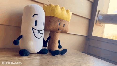 Two Stuffed Animals Are Sitting On A Table And One Has A Crown On His Head GIF