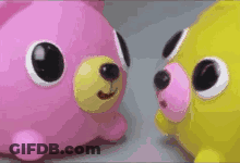 Two Stuffed Animals , One Pink And One Yellow , Are Standing Next To Each Other . GIF