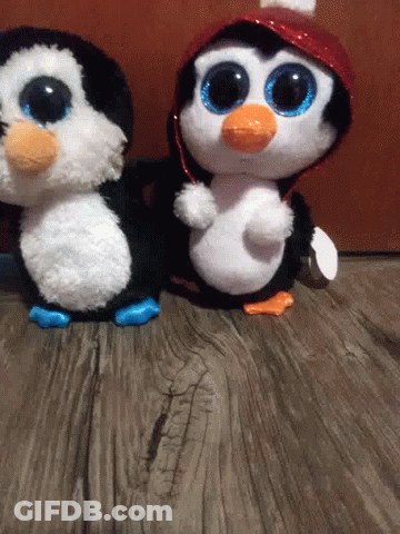 Two Stuffed Penguins Are Standing Next To Each Other On A Wooden Table . GIF